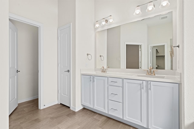 bathroom featuring double vanity, visible vents, a sink, wood finished floors, and baseboards