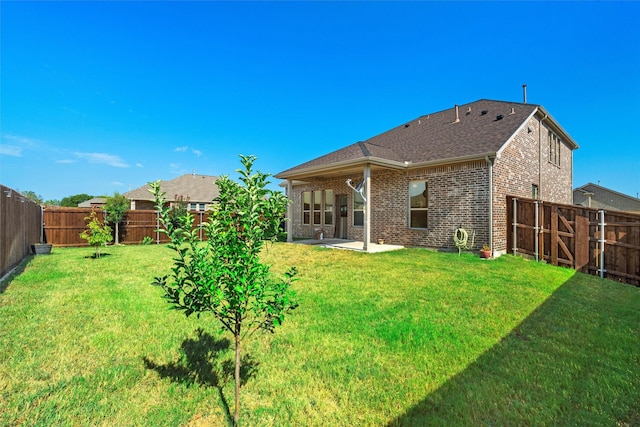 back of property with brick siding, a fenced backyard, a yard, and a patio