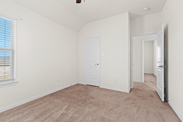 unfurnished bedroom featuring light carpet, ceiling fan, baseboards, and vaulted ceiling