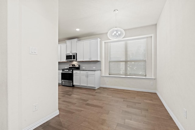 kitchen with light wood-style flooring, white cabinetry, hanging light fixtures, appliances with stainless steel finishes, and backsplash