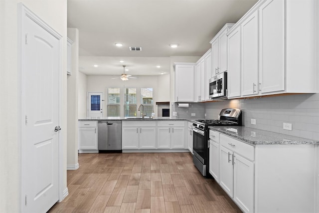 kitchen with stainless steel appliances, visible vents, decorative backsplash, white cabinets, and a sink