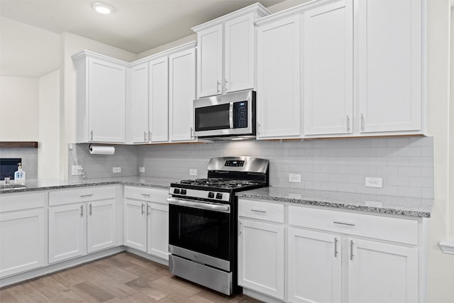 kitchen featuring light stone counters, stainless steel appliances, decorative backsplash, light wood-style floors, and white cabinets