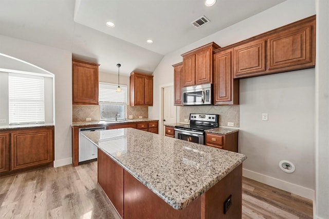 kitchen with appliances with stainless steel finishes, pendant lighting, light stone counters, and a kitchen island