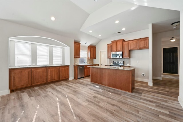 kitchen featuring stainless steel appliances, backsplash, lofted ceiling, light stone countertops, and a kitchen island