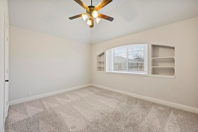 carpeted empty room with ceiling fan, built in shelves, and lofted ceiling