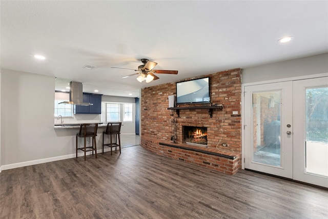 living room with french doors, dark hardwood / wood-style floors, ceiling fan, and a brick fireplace