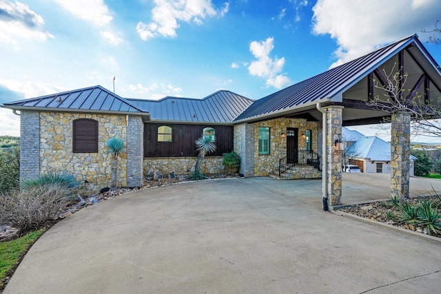 view of front of house with a standing seam roof, stone siding, metal roof, and concrete driveway