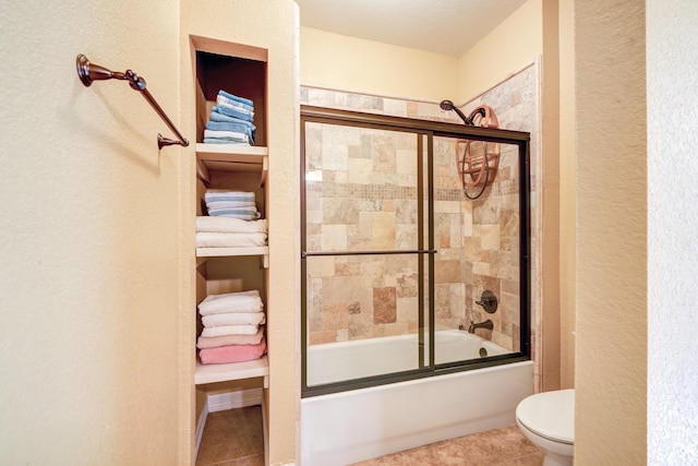 bathroom featuring enclosed tub / shower combo, a textured wall, tile patterned flooring, and toilet