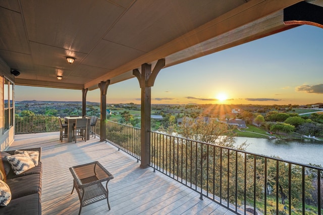 deck at dusk with outdoor dining space and a water view