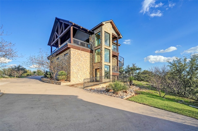 view of home's exterior with stone siding, a lawn, and a balcony