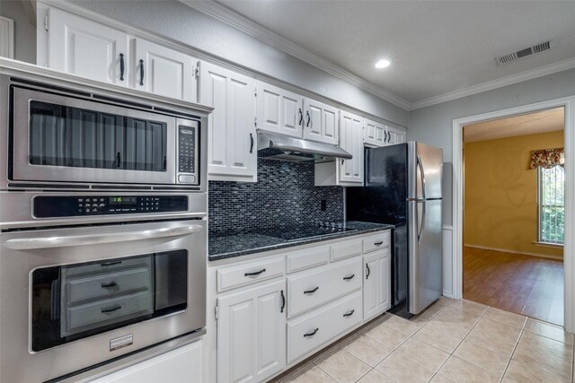 kitchen with white cabinets, light tile patterned floors, backsplash, appliances with stainless steel finishes, and crown molding