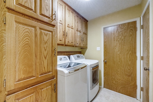 laundry room featuring cabinets, a textured ceiling, light tile patterned floors, and washing machine and dryer