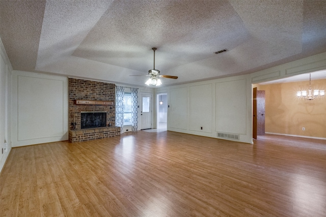 unfurnished living room featuring a textured ceiling, ceiling fan with notable chandelier, light hardwood / wood-style floors, and a fireplace