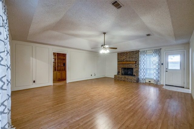 unfurnished living room featuring light wood-type flooring, built in shelves, a brick fireplace, a raised ceiling, and ceiling fan