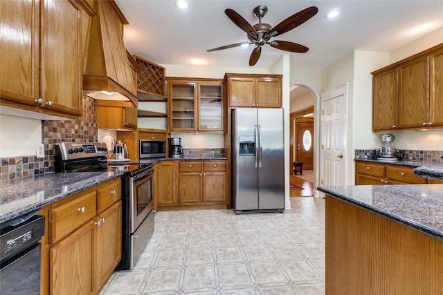 kitchen with ceiling fan, stainless steel appliances, dark stone countertops, decorative backsplash, and custom exhaust hood