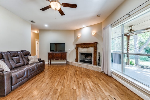 living room with a tile fireplace, a wealth of natural light, ceiling fan, and light hardwood / wood-style floors