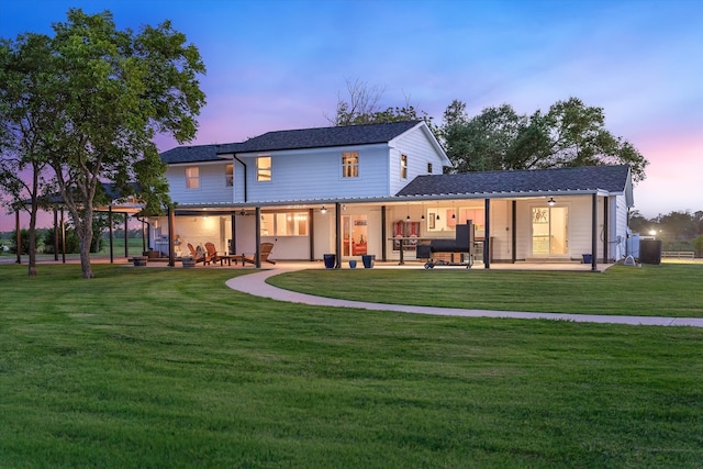 back house at dusk featuring a lawn