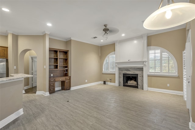 unfurnished living room with ceiling fan, ornamental molding, light wood-type flooring, and a fireplace