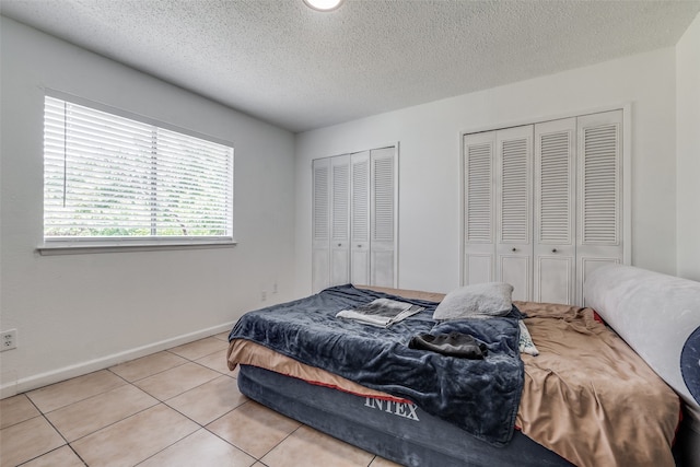 bedroom with multiple closets, light tile patterned floors, and a textured ceiling