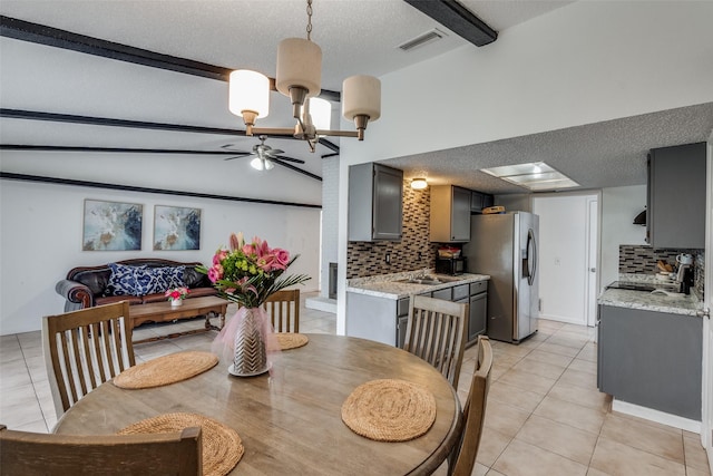 dining area featuring ceiling fan with notable chandelier, lofted ceiling with beams, a textured ceiling, and light tile patterned floors