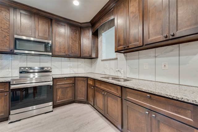 kitchen with tasteful backsplash, range with electric stovetop, sink, light wood-type flooring, and light stone countertops