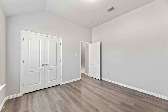 unfurnished bedroom featuring hardwood / wood-style flooring, lofted ceiling, and a closet