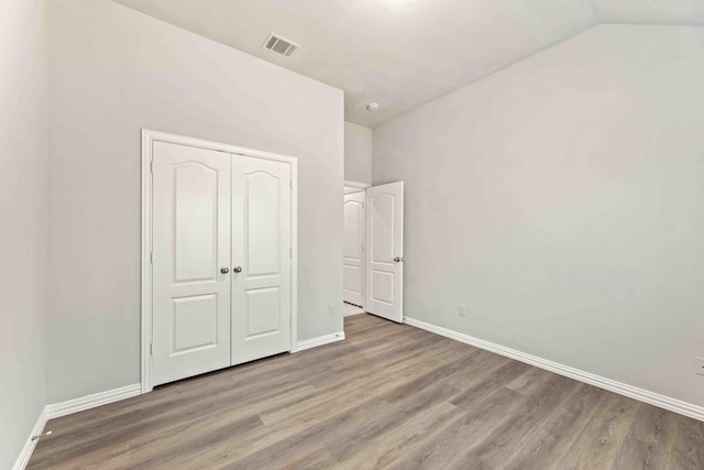 unfurnished bedroom featuring wood-type flooring, vaulted ceiling, and a closet