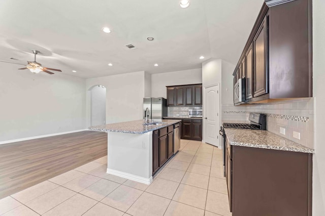 kitchen with ceiling fan, tasteful backsplash, appliances with stainless steel finishes, light tile patterned floors, and a kitchen island with sink