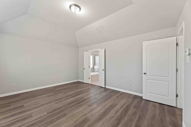 unfurnished bedroom with ensuite bathroom, vaulted ceiling, and dark wood-type flooring