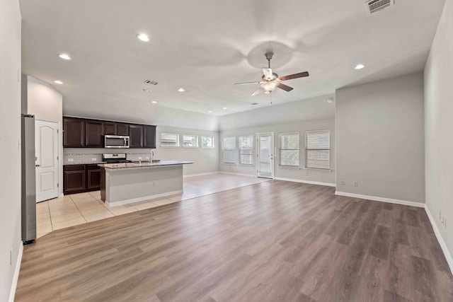 kitchen with light hardwood / wood-style floors, appliances with stainless steel finishes, a center island with sink, and ceiling fan