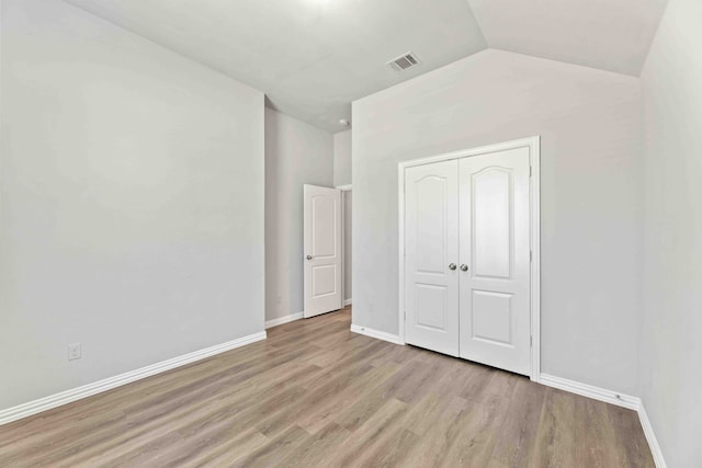 unfurnished bedroom featuring hardwood / wood-style flooring, vaulted ceiling, and a closet