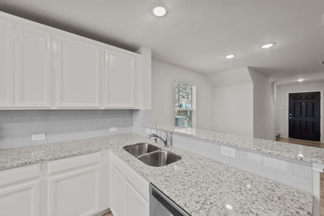 kitchen with white cabinetry, kitchen peninsula, light stone counters, decorative backsplash, and sink