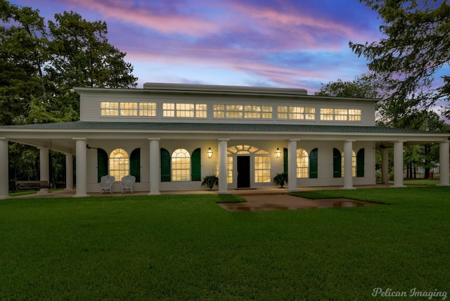 back house at dusk featuring a porch and a yard