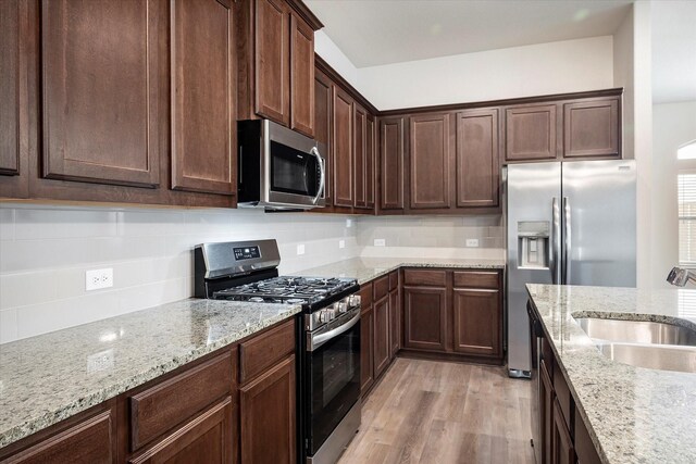 kitchen featuring decorative backsplash, sink, light stone countertops, appliances with stainless steel finishes, and light hardwood / wood-style flooring