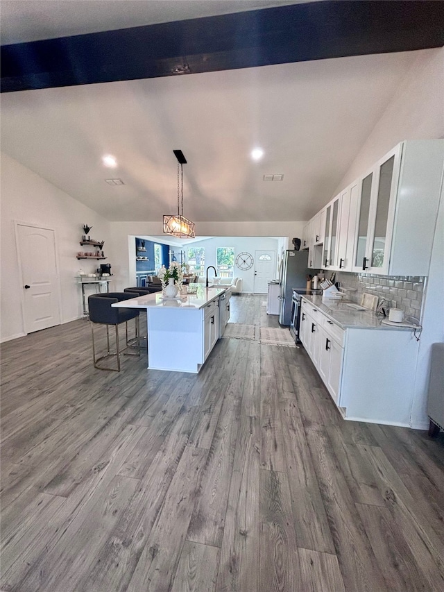 kitchen with decorative backsplash, white cabinets, hardwood / wood-style floors, an island with sink, and decorative light fixtures