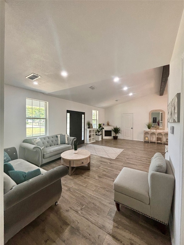 living room featuring vaulted ceiling with beams, a textured ceiling, and light wood-type flooring