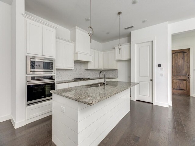 kitchen featuring white cabinetry, dark hardwood / wood-style flooring, an island with sink, appliances with stainless steel finishes, and sink