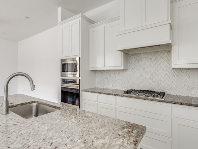 kitchen with white cabinetry, custom range hood, tasteful backsplash, light stone counters, and appliances with stainless steel finishes