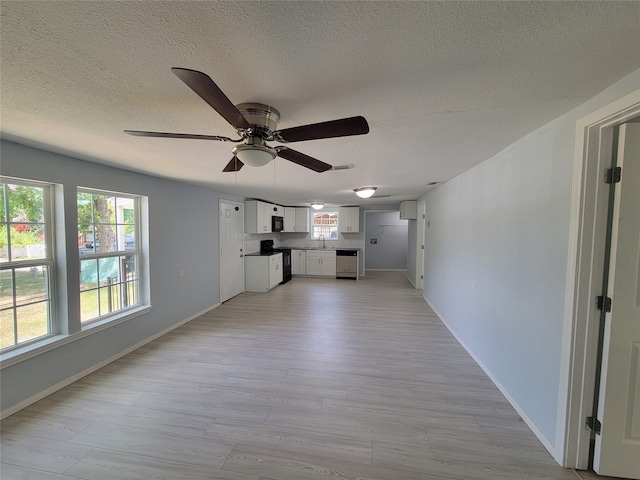 unfurnished living room with sink, light hardwood / wood-style flooring, a textured ceiling, and ceiling fan