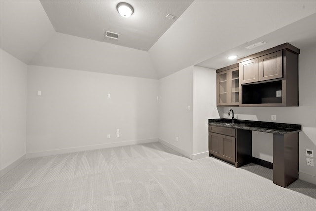 kitchen featuring dark stone countertops, vaulted ceiling, sink, and light colored carpet