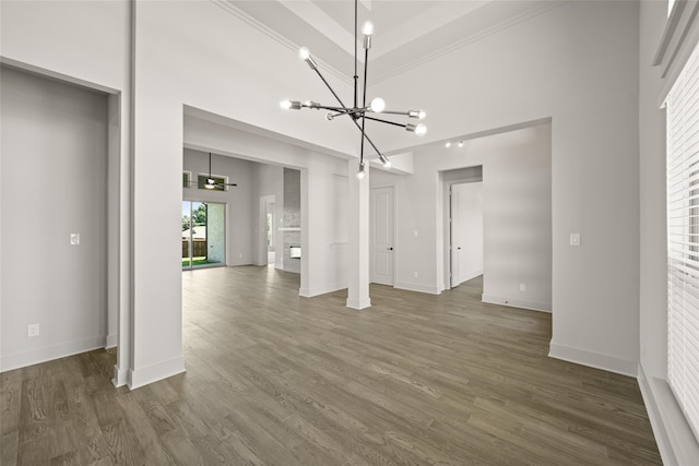 unfurnished dining area with ornamental molding, dark wood-type flooring, a notable chandelier, and a towering ceiling