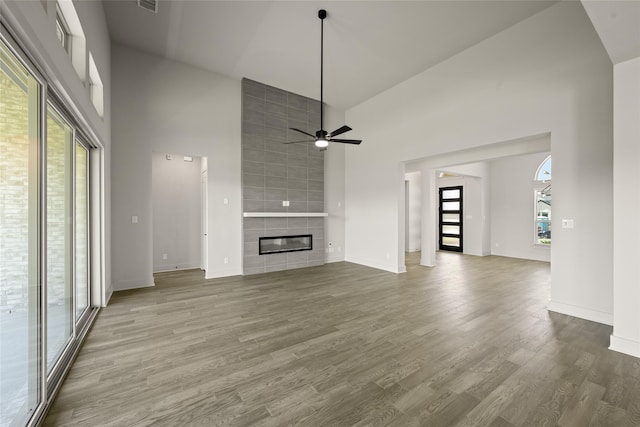 unfurnished living room featuring high vaulted ceiling, ceiling fan, a tile fireplace, and wood-type flooring