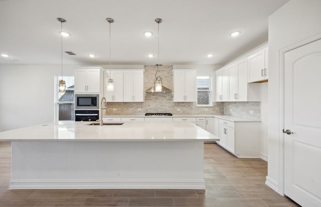 kitchen featuring white cabinets, a center island with sink, hanging light fixtures, black appliances, and sink