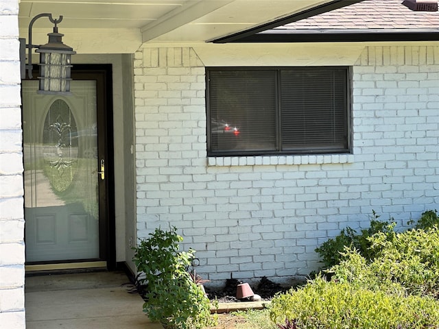 doorway to property featuring brick siding and roof with shingles