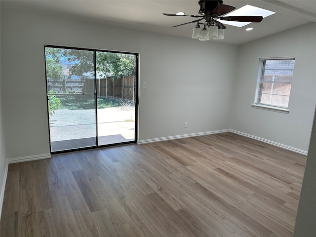 unfurnished room with ceiling fan, lofted ceiling with skylight, and hardwood / wood-style floors