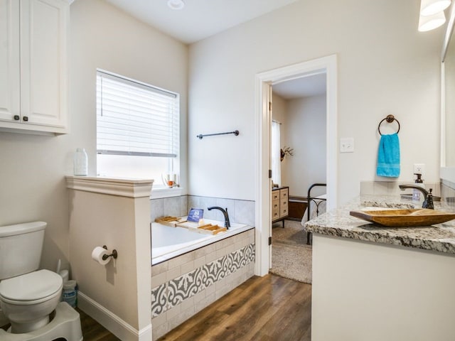 bathroom featuring toilet, wood finished floors, vanity, baseboards, and a bath