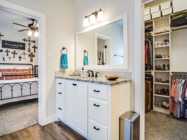 ensuite bathroom featuring a walk in closet, a ceiling fan, vanity, ensuite bath, and wood finished floors