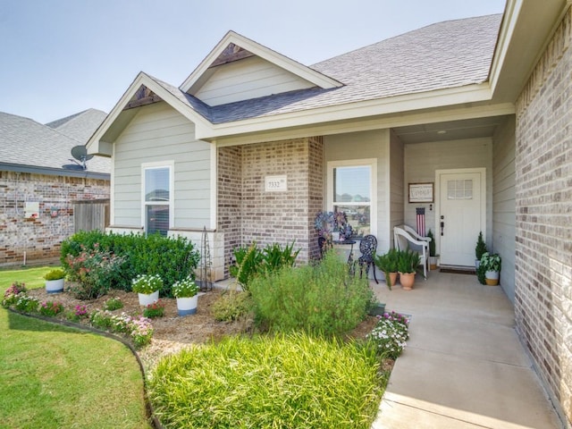 view of exterior entry featuring brick siding and roof with shingles