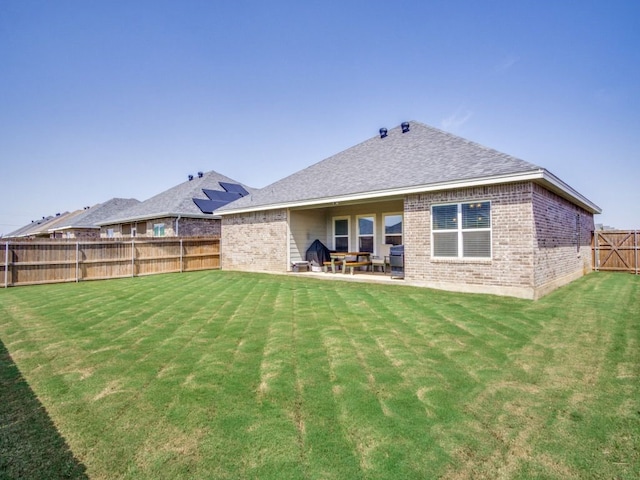 rear view of house featuring brick siding, a yard, a fenced backyard, and a patio