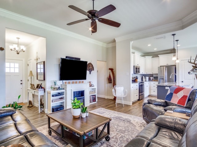 living room with light wood-type flooring, ceiling fan with notable chandelier, and ornamental molding